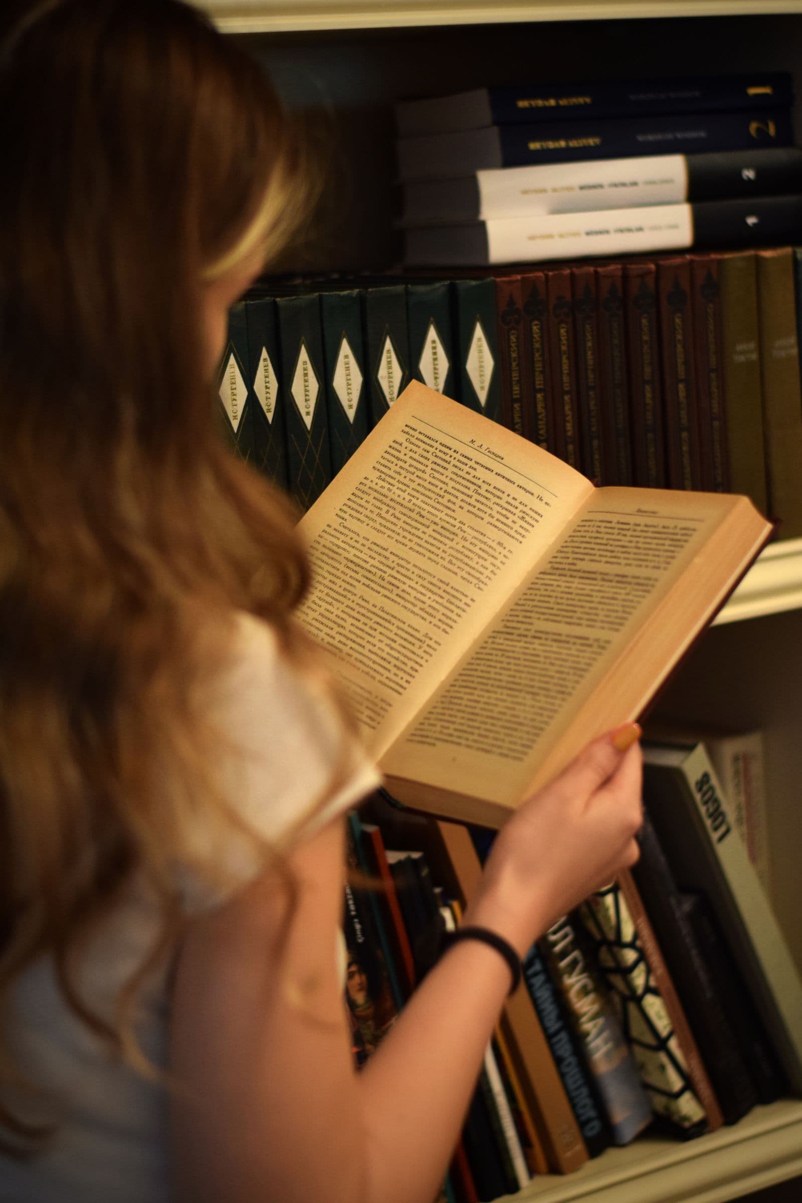 A woman reading beside a shelf of books